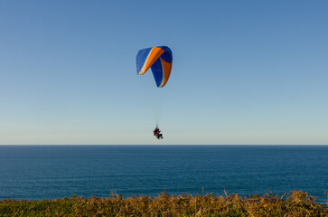 Sunset over the sea in Basque country with people doing paragliding
