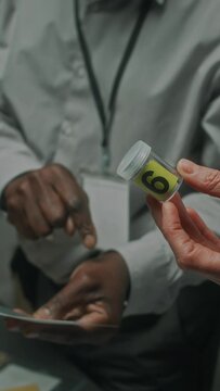 Close-up vertical shot of hands of anonymous diverse male and female police detectives or federal agents holding container with sample from murder scene, pointing to victim photo