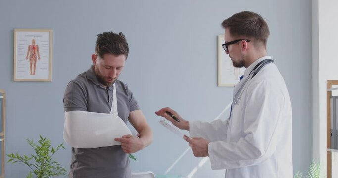 Male patient with a broken arm talking with a doctor or nurse during a hospital visit consultation. The medical professional provides care, advice and support regarding the arm trauma.