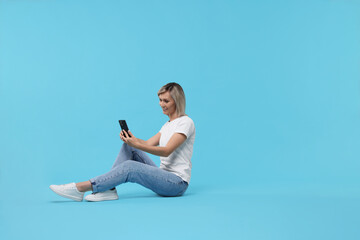 Happy woman with phone on light blue background, space for text