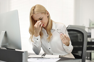 Overwhelmed woman with glasses at table in office