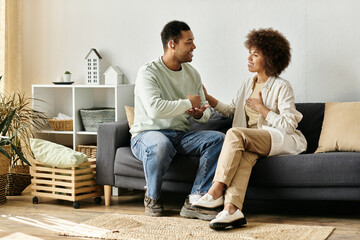 An African American couple sits on a couch in their home, communicating with sign language.