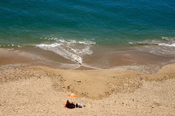 Obraz premium Lagos, Faro district, Algarve, Portugal, Europe - Couple relaxing under sun umbrella on beautiful sandy beach - Porto de Mos seen from high cliff above
