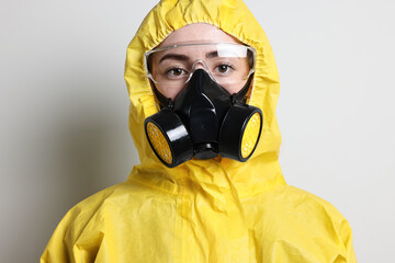 Worker in respirator, protective suit and glasses on grey background