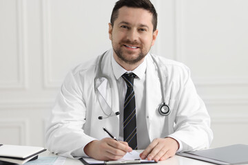 Fototapeta premium Doctor with pen and clipboard working at white table in clinic