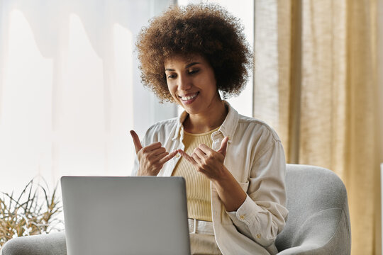 A woman signs with a smile while sitting at her laptop in a home office.