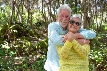 Happy active senior family couple enjoying mountain hike in the forest appreciating nature and freedom, retired seniors hug expressing love and care
