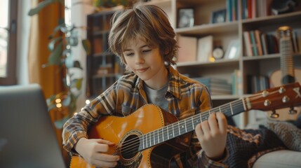 A diligent Caucasian boy of 10 years of age is learning to play the guitar online while sitting at a laptop monitor while at home. learning to play guitar remotely