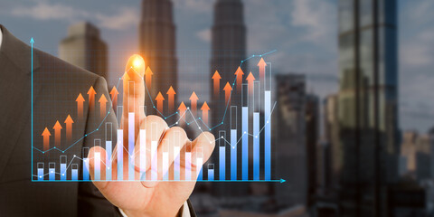 Close up of businessman hand pointing at growing business graph on blurry city background....
