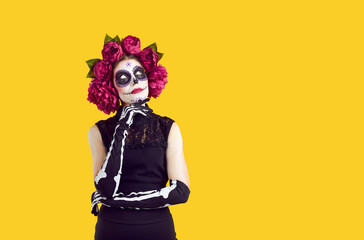 Artist in Halloween and Day of the Dead carnival costume looks at virtual goods space to her left. Thoughtful zombie making a choice. Creepy ewening make up, isolated image on yellow background.