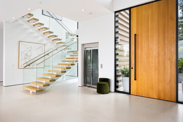Room with stairs, a large door and an elevator inside a luxurious modern house with white walls