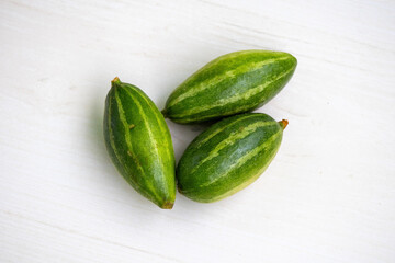 Fresh green vegetable pointed gourd or potol isolated on light wooden background. It is also known...