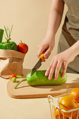 A green squash placed on wooden chopping, cut by a yellow knife hold in female hand, in front as a...
