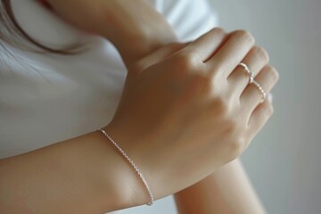 A close-up of a cute girl's long, slender fingers adorned with a delicate silver chain bracelet, set against a plain white background