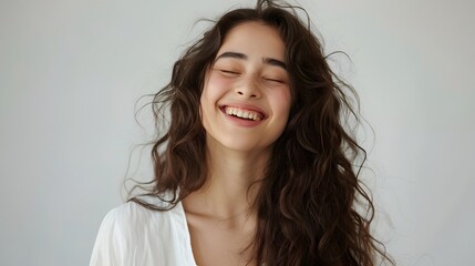 Fototapeta premium A woman with long hair laughing and smiling, wearing white , against a light background. creating an atmosphere filled with warmth and positivity.
