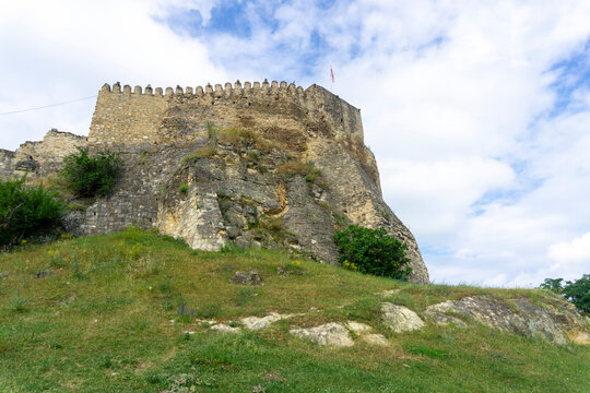 Side view of Surami fortress built on a rock. Green grass, stone walls with loopholes