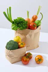 Advertising template from high angle shot, two brown paper bag contains fresh vegetable, placed on white table, beside it is some ripe tomatoes. Empty space for designing