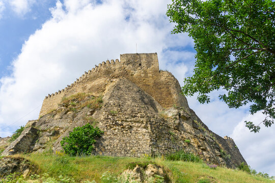 Front view of Surami fortress on the rock. Stone tower, wall with loopholes. Bright blue sky with clouds