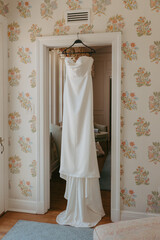 White bridal gown on a door near a bed
