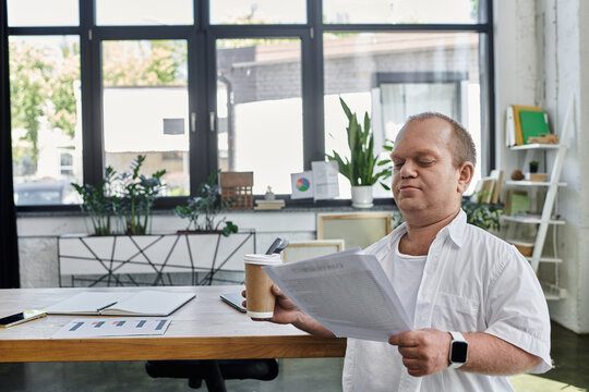 A man with inclusivity reviews paperwork at a desk in a modern office setting.