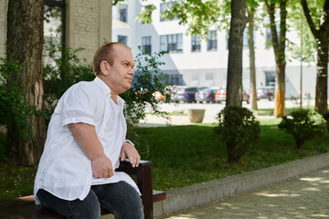 Obraz premium A man with inclusivity sits on a bench in a city park, surrounded by greenery.