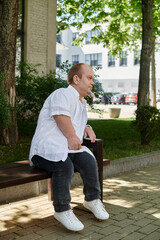 A man with inclusivity sits on a bench in a park, gazing off into the distance.