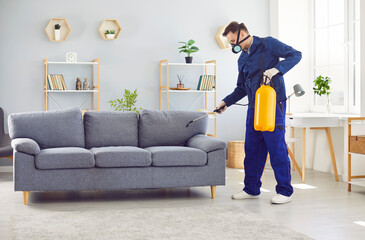 Man from the pest control service diligently sprays insecticide on the sofa in the living room at...