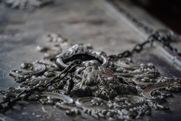 Dobele, Latvia - June 7, 2024 - Close-up of an ornate, weathered metal lock with a chain on a decorative surface, showcasing intricate designs and textures.