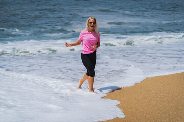 A joyful girl of European appearance in a pink T-shirt on the beach of Nazaré in Portugal on the shores of the Atlantic Ocean on a summer day.