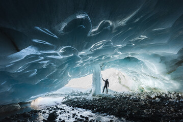 Winter landscape view of an alpinist exploring an ice cave with a frozen waterfall
