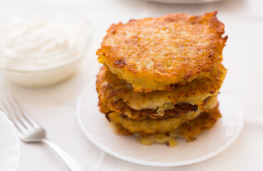 Fried grated potato pancakes with sour cream on white plate