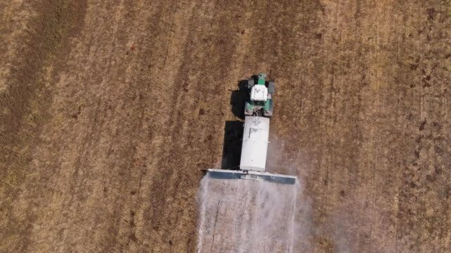 Aerial footage of a tractor working on an agricultural field spraying lime to the natural soil