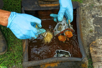 cleaning and washing with a brush in a plastic canister of gasoline with hands in blue rubber...