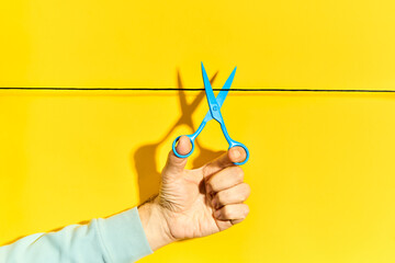 Male hand holding scissors and cutting rope on yellow background
