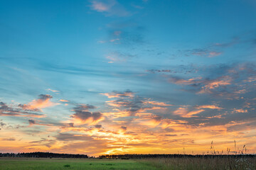 Obraz premium scenic landscape photograph captures a captivating sunset, showcasing a vibrant sky painted in hues of orange, pink, and blue, with wispy clouds streaking across the horizon.