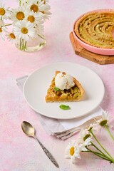 Cut tart on a sand dough with rhubarb and walnuts laid out in a circle on a white plate on a pink...