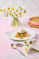 Cut tart on a sand dough with rhubarb and walnuts laid out in a circle on a white plate on a pink concrete background.