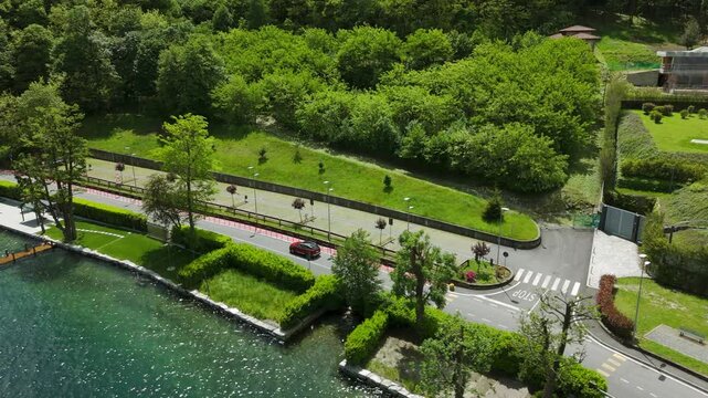 Red car driving on panoramic road along Orta Lake, Pella town in Italy.