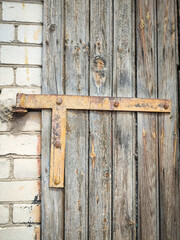 Texture of a wooden plank back door with triangular metal detail between white brick wall and wooden part, brown wooden door connection