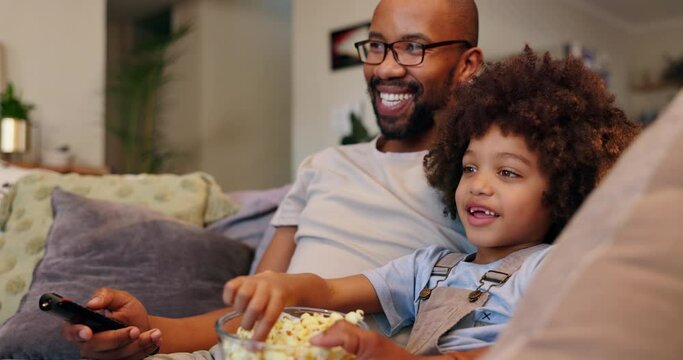 Happy dad, child and watching tv with popcorn for movie, entertainment or bonding on sofa at home. Father, kid or young little boy with remote for online streaming or cartoon in living room at house