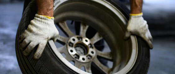 Auto mechanic in gloves holding car wheel in garage, web banner