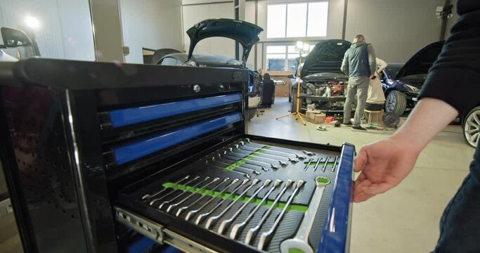 A mechanic handling tools and working on an electric car in a well-lit auto repair shop with blue tool cabinet. EV repair concept. Auto Service, Electric vehicle engine maintenance