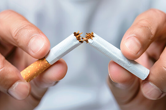 Conceptual image of a man breaking a cigarette in half, set against a blurred background, symbolizing the decision to quit smoking and embrace a healthier lifestyle - Powered by Adobe