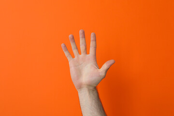 Male hand showing five fingers on orange background