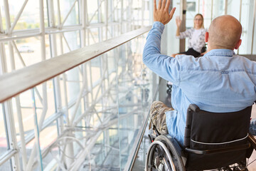 Man in wheelchair greeting a woman in a modern glass building