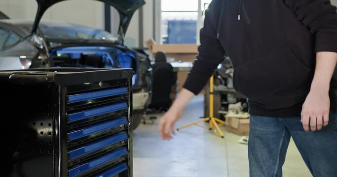 Mechanic opening a toolbox drawer in an electric car repair workshop, focusing on maintenance and repair tasks. EV repair concept. Auto Service, Electric vehicle engine maintenance