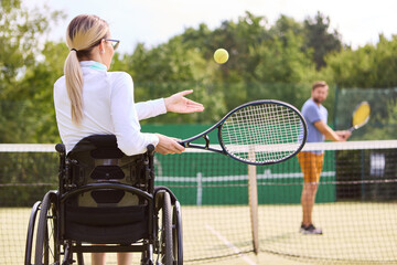 Woman in wheelchair playing tennis with partner on outdoor court