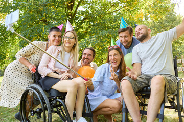 Group of joyful friends with party hats taking a selfie, including person in wheelchair celebrating outdoors