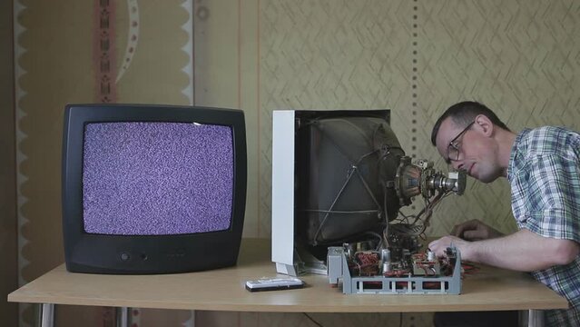 A television technician repairs an outdated tube TV. An electrician checks the TV with a tester and cleans it from dust.