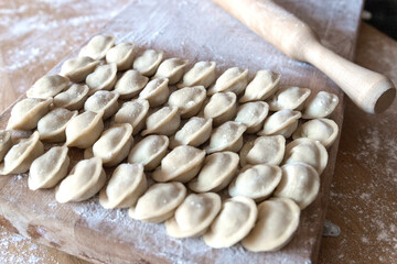 Raw dumplings were laid out on a wooden board for cooking. Next to it is a rolling pin for rolling out the dough. The filling is minced meat, potatoes, cheese or cottage cheese.